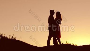 恋爱中的情侣在日落时跳舞剪影和自然接吻。 爱的男人和女人与狗跳舞剪影缓慢